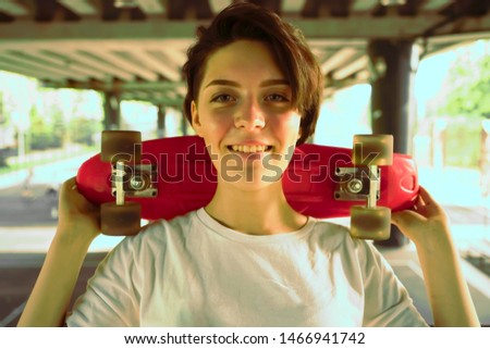 Portrait of a young happy beautiful woman with short hair. hipster girl in white t-shirt holding skateboard on shoulder. bridge background.Copy space.Lifestyle concept.