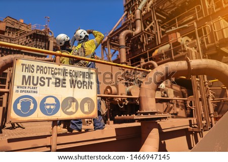 Personal protective equipment (PPE) must be worn sign with defocused of construction workers wearing white hard hat at the background while working on live refinery plant construction site Perth