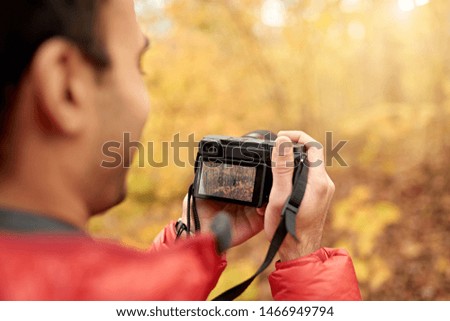 Attractive indian man taking pictures with a mirrorless camera through the forest in the fall in Canada