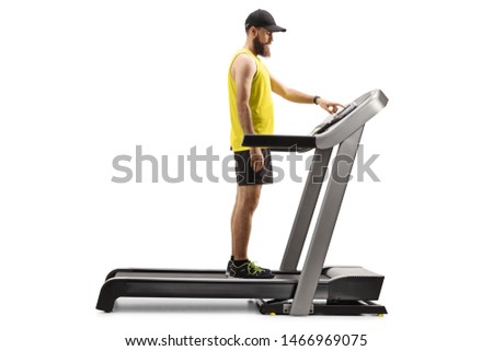 Full length shot of a bearded guy in sportswear standing on a treadmill and pressing a button isolated on white background