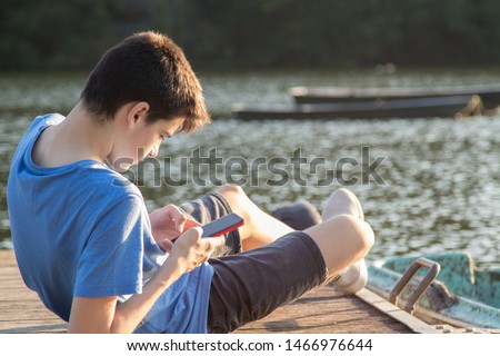 young man with mobile phone on the jetty at sunset