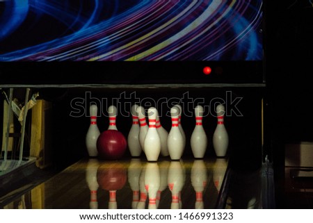 Rolling red ball knocks down pins on a bowling alley lane