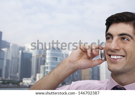 Closeup of happy young businessman using cellphone with cityscape in background