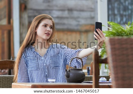 Young happy smiling girl wearing blue shirt, using phone in the Asian style cafe against blurred background