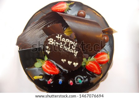 chocolate cake with strawberry slices, and chocolate with a happy birthday greeting. From top view on white background