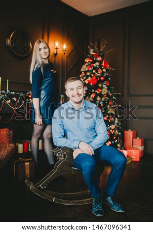 Handsome man on wooden horse swing near christmas decorated tree with her girl. Vertical portrait