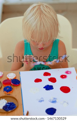 Cute blond girl with painted hands drawing with stamps 