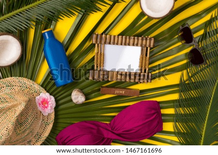 Beach theme on yellow background. Photo frame, hat, coconut, swimsuit, palm leaves, on  yellow background. Top view.