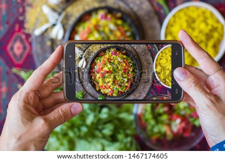 Photo of food in cafe with phone. Finger tap a screen to shoot a lunch in Arabic restaurant - tabbouleh with bulgur.