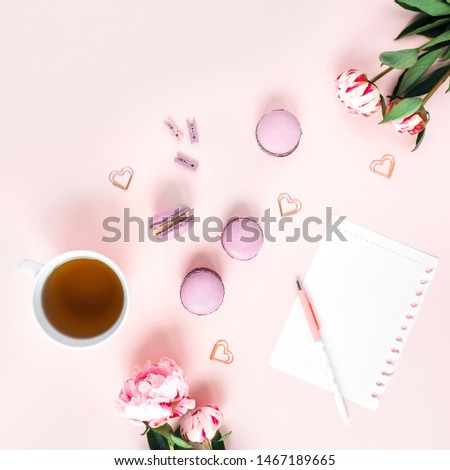 Pink background with macaroons and a Cup of tea surrounded by peonies. Top view.