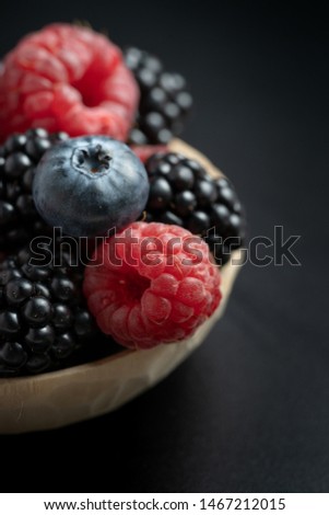 Vertical photo and close up view of mix different ripe and sweet blueberries, blackberries, raspberries fruits in wooden bowl on black background with copy space