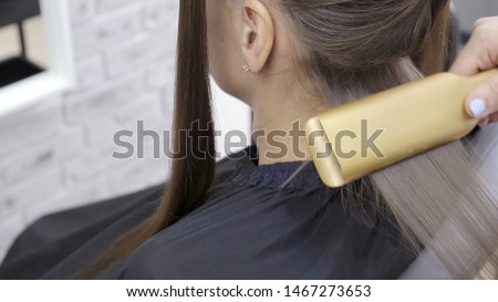 Cute girl with long brunette hair hairdresser doing hair lamination in a beauty salon. concept of hair care treatment. 