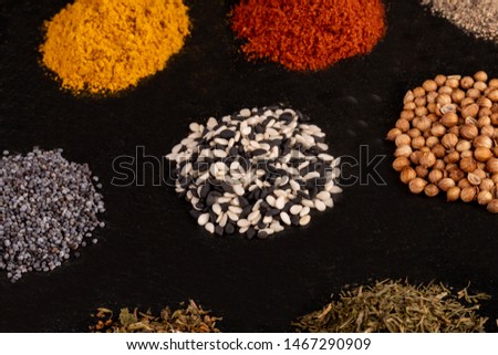 Different piles of spices isolated on black stone plate plaque. Place for text copy space. Various types of condiments directly on a dark stone background. View from top and side. powder and seeds mix