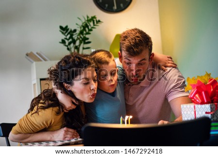 Happy family celebrating a birthday together at home. Young parents with son blowing candles on cake.