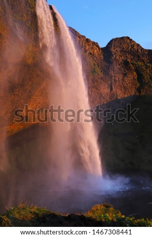 A scenic view of Seljalandsfoss - one the most famous and visited falls in Iceland. Cascade of water falls from a tall cliff at sunset.