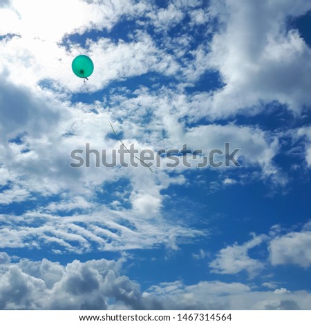 Green balloon flies into the clouds. Blue sky with feathery clouds.