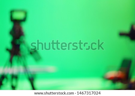 Blurred images of video cameras and chairs in a TV studio  With a green screen background