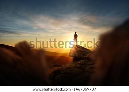 Leadership And Goals. A man standning on top of a mountain watching the sun set. Conceptual photo composite.