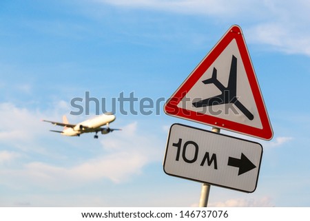 road sign "Caution low-flying aircraft" on a background of blue sky and aircraft with the gear