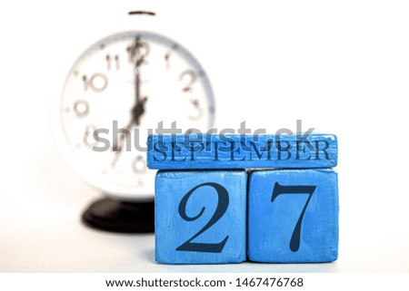 september 27th. Day 27 of month, handmade wood cube calendar and alarm clock on blue color. autumn month, day of the year concept.