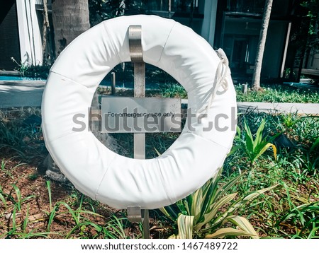 White lifebuoy with inscription «for emergency use only” in green garden with swimming pool