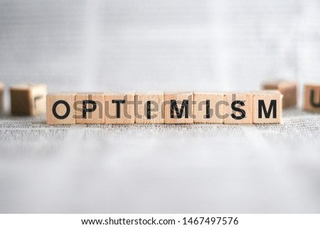optimism Word Written In Wooden Cube with Newspaper Background Concept