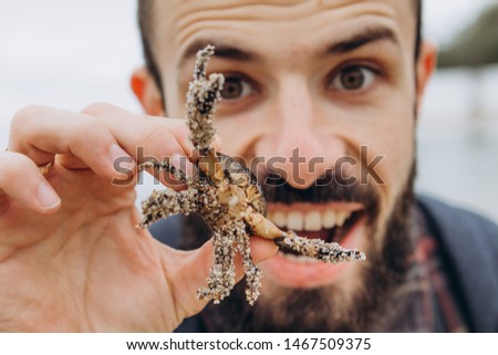A cool picture of a man who holds a small crab in his arms while walking along the sea in cloudy cold weather