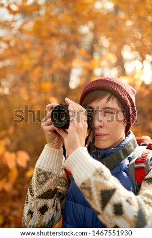 Attractive caucasian girl taking pictures with a mirrorless camera through the forest in the fall in Canada