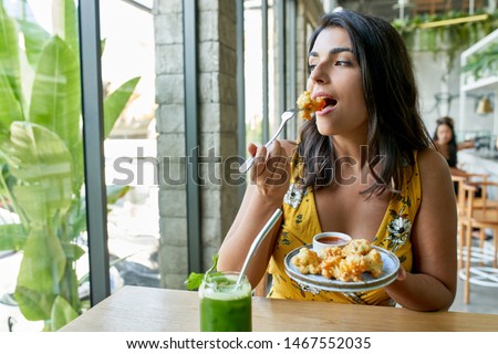 Candid lifestyle portrait of fashionable healthy ethnic businesswoman eating an organic vegetarian cauliflower dish for vegans and drinking green smoothie Royalty-Free Stock Photo #1467552035