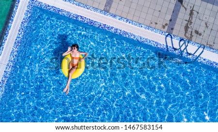Beautiful young woman in hat in swimming pool aerial top view from above, girl in bikini relaxes and swims on inflatable ring has fun in water on family vacation, tropical holiday resort