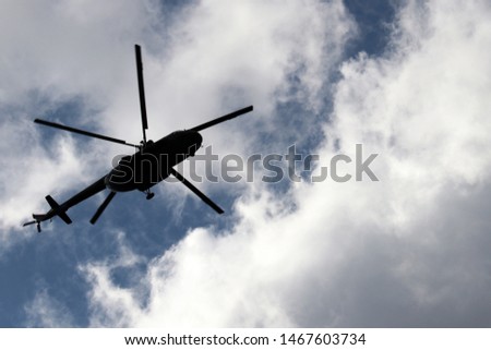Helicopter silhouette in flight on background of blue sky with white clouds. Bottom view, air transportation concept