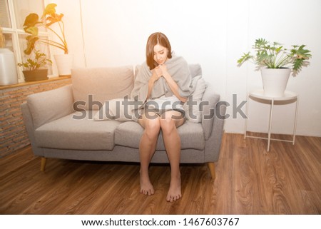 Asian woman sad suffering from cold Due to fever on the sofa in a room.