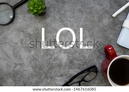 Top view of magnifying glasses,plant,sunglasses,a cup of coffee,notebook and pen on grey floor background written with LOL.