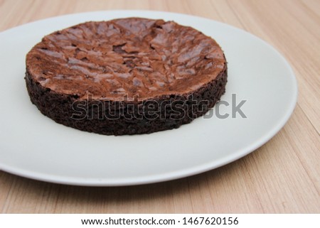 A picture of homemade brownie, which is shiny on top, is on the white plate.