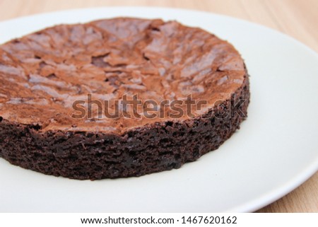 The close up picture of homemade brownie, which is shiny on top, is on the white plate.