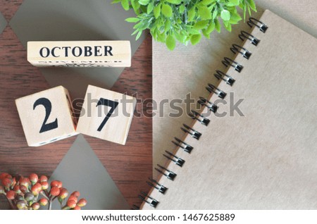 October 27. Date of October month. Number Cube with a flower and notebook on Diamond wood table for the background.