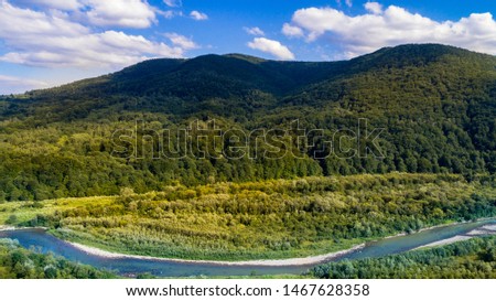 Aerial view of perfect green valley wit dramatic blue sky and hills covered by green forest and small spring river 