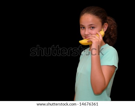 Young girl holding a banana like a telephone on a black background