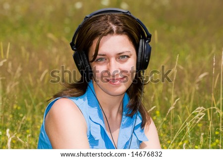 Attractive young woman listening music in a grass field