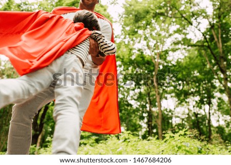 low angle view of father spinning little boy in red superhero cloak