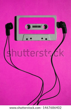 Top view of black earphone and gray classic tape cassette against violet  isolated background. Listening music theme.