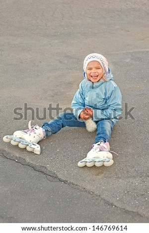 Little beautiful smiling girl with rollers sitting on the pavement.
