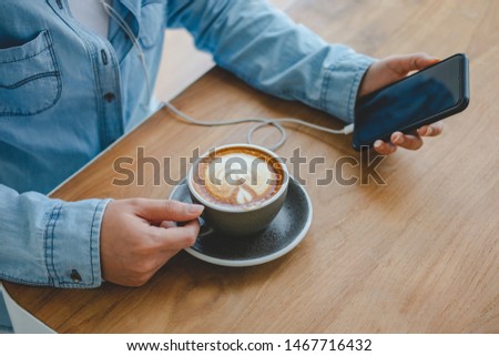 Women hands holding cup of coffee and listening to music on smart phone in coffee shop.
