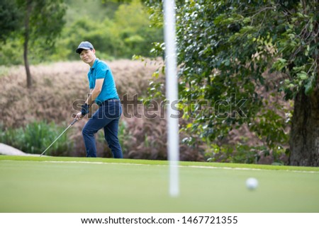 The male golfer is aiming a golf ball on the pitch.