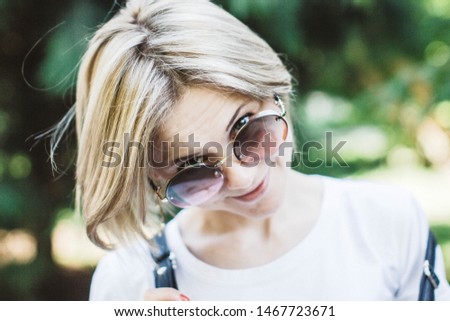 Portrait of a cute charming blonde with a short haircut and sunglasses. Cheerful smiling young woman in natural daylight