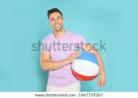 Happy young man with bright inflatable ball on blue background