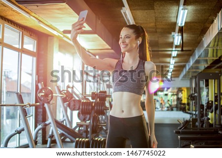 Beautiful young fit woman taking selfie photo using her smartphone after sports training in gym
