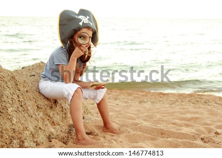Caucasian emotional little girl in a hat with a symbol of maritime piracy keeps pirate treasure map on the background of the sea
