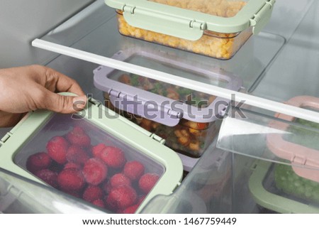 Woman taking box with frozen strawberry from refrigerator, closeup