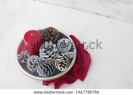 winter christmas still life with red candle silver cones and serviette fabric on white background
